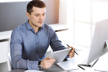 Businessman working with computer in modern sunny office. Headshot of male entrepreneur or company director at workplace. Business concept