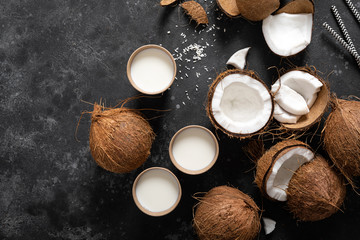 Wall Mural - Coconut milk, whole and cracked coconuts on black background, top view