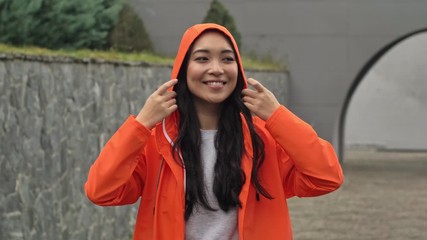 Wall Mural - Young asian beautiful positive woman walking outdoors in orange coat.