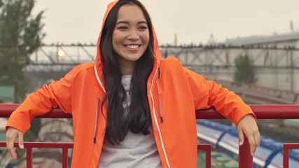 Wall Mural - Pretty asian happy positive woman walking by harbor grant outdoors in orange coat.