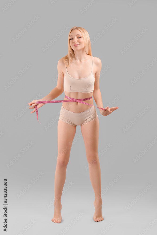 Slim woman with measuring tape on grey background. Weight loss concept
