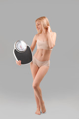 Wall Mural - Slim woman with scales on grey background. Weight loss concept