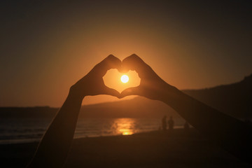 silhouette of two hands forming a heart during sunset