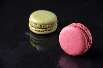 Top view of pink and green macaron, with selective focus, on wet slate stone, with reflection, horizontally, with copy space