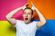 © DSMT - portrait of a young cheerful guy on a multi-colored background, dressed in a white T-shirt, poured hair foam in his hands, creates a fashionable hairstyle