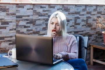 Pensive student girl using laptop while sitting outdoors at home terrace.