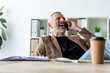© LIGHTFIELD STUDIOS - selective focus of cheerful businessman talking on smartphone near paper cup