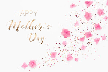 Wall Mural - Gold glitter confetti and pink flowers on white background. Spring Holidays frame. Text Happy Mothers Day card.