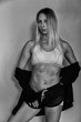 © Inception - Sports muscular woman portrait wearing black sportswear over grey. Attractive sexy caucasian woman with long blond hair in studio shot.