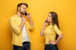 © LIGHTFIELD STUDIOS - Skeptical couple talking on smartphones on yellow background