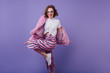 © Look! - Smiling european lady in trendy sunglasses dancing in fur jacket. Studio shot of beautiful female model with wavy brown hair jumping during photoshoot.