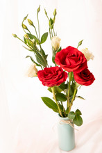 Three Red Roses And A White One Stand Against A Pink Curtain