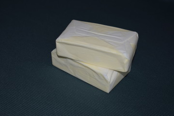 Two packs of butter on a dark green tablecloth. Dairy product in parchment packaging.