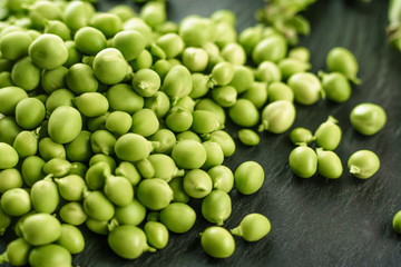 Macro close up view of fresh shelled peas on a black slate plate. Black and green contrast from healthy vegan cuisine, the freshness of the nature