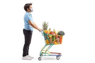 Wall Mural - Kid with a protective mask standing with a shopping cart filled with healthy food