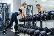 © Vadim - Full length portrait of young fit sporty girl posing near shelf with metal dumbbells. Cute slim woman wear cap and sports cloth look at camera along wall with mirror reflection