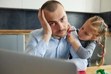 Wall Mural - Father Working from home on laptop during quarantine. Little child girl make noise and distracts father from work on the kitchen office