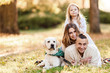 © zadorozhna - Happy family is having fun with dog labrador are lying on green grass in park.