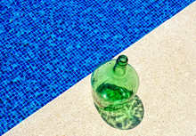 High Angle View Of Green Empty Bottle At Poolside During Sunny Day