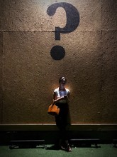 Woman Using Phone While Standing Below Question Mark On Wall At Night