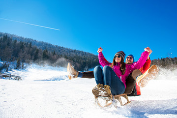 Young happy couple sledding in winter at ski center