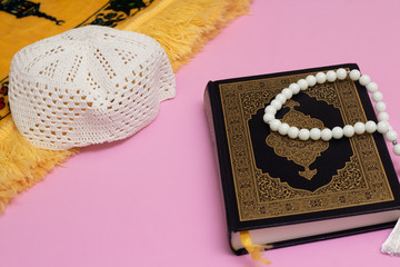 Wall Mural - Quran with skullcap and muslim rosary and prayer rug on a pink background