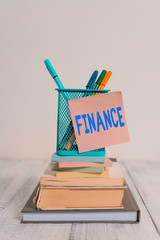 Poster - Handwriting text Finance. Conceptual photo Management of large government companies money amount Provide funds Stacked books pens metal holder sticky note lying vintage old wooden table