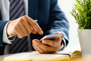 Male arm in suit hold phone and silver pen at workplace closeup. Read news mania send sms chat addict use electronic bank modern lifestyle job plan colleague share blog tweet web application search