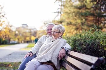 Mature couple sitting on bench in public park talk and smile