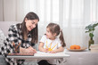 © puhimec - A mother with a child sits at the table and does homework. The child learns at home. Home schooling.