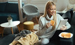 © Drazen - Happy woman using touchpad and eating waffles in the living room.