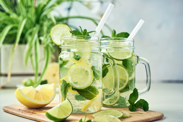 Two glasses of homemade lemon, lime, and mint lemonade sit on the wooden dining table. Cold, refreshing summer lemonade or mojito.