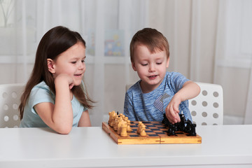 A little girl and a boy sit at a table and play chess