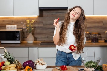 Healthy Food - Vegetable Salad. Diet. Dieting Concept. Young curly woman preparing vegetable salad in her kitchen. Healthy lifestyle concept, beautiful smiling woman eat sweet red pepper.