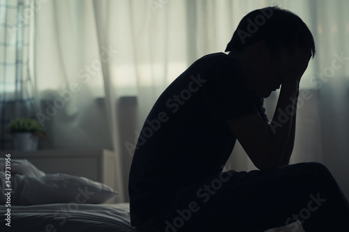 Depressed lonely man sitting alone on the bed with hands on head feel stress, sad and worried in the dark bedroom and low light environment.