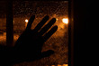 Hand resting on the window at night with the warm light of the street lamps and with drops of water from a rainy day. Sad image of melancholy looking out from the sleeping room.