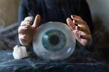 Fortune Teller Holds Hands Above Magic Crystal Ball With Eyeball Inside. Conceptual Image Of Black Magic And Occultism