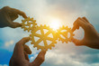 © gerasimov174 - Three hands of businessmen assemble gears into a puzzle in a single whole against the backdrop of the sunset, business concept idea, partnership, teamwork, cooperation, creative