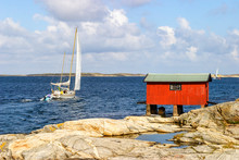 Sailboat At Sea With A Red Boathouse On The Rocks In The Archipelago