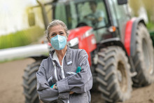 Female Farmer Standing In Front Of A Tractor And Wearing A Protective Mask Against Covid-19