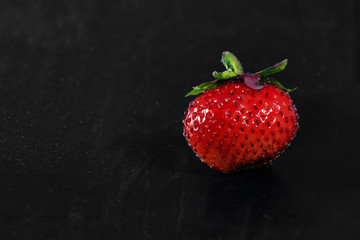 one strawberry on a black wooden background