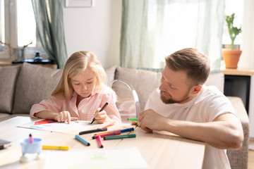 Wall Mural - Happy young father in casualwear looking at his cute little daughter drawing