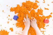 Orange Magic Sand In A Kids Hands On A White Background Close Up. Early Sensory Education. Preparing For School. Development