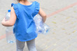 © Inna - Faceless little girl holding plastic water bottles for recycling. Back view. Concept plastic free world, zero waste.