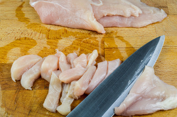 Chopped raw chicken breasts and knife on a wooden chopping board