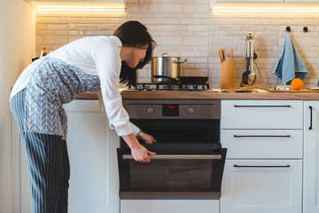 young pretty woman open oven to cook. domestic kitchen concept