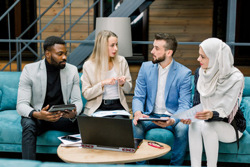 Focused confident multi ethnic businesswomen and businessmen making SWOT analysis, discussing benefits and disadvantages of their joint business project in the modern office room