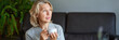 © JENOCHE - Delicious drink.Elderly woman sitting on the sofa in her living room and holding a cup of coffee