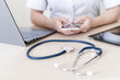 © Михаил Решетников - Unrecognizable female doctor sits at a desk and uses a smartphone. Closeup of the hands of a practitioner with a phone. Stethoscope tablet and laptop on the table.