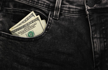 Hundred dollar bills in the front pocket of black jeans close-up.